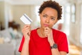 Young african american woman holding credit card serious face thinking about question, very confused idea