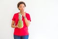 Young african american woman holding fresh healthy pineapple fruit cover mouth with hand shocked with shame for mistake,