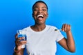 Young african american woman holding glass of mouthwash and toothbrush for fresh breath smiling and laughing hard out loud because Royalty Free Stock Photo