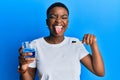 Young african american woman holding glass of mouthwash and toothbrush for fresh breath sticking tongue out happy with funny Royalty Free Stock Photo