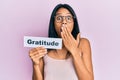 Young african american woman holding gratitude message paper covering mouth with hand, shocked and afraid for mistake