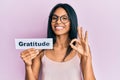 Young african american woman holding gratitude message paper doing ok sign with fingers, smiling friendly gesturing excellent