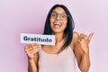 Young african american woman holding gratitude message paper pointing thumb up to the side smiling happy with open mouth