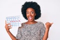 Young african american woman holding heart calendar pointing thumb up to the side smiling happy with open mouth