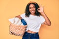 Young african american woman holding laundry basket doing ok sign with fingers, smiling friendly gesturing excellent symbol