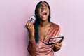 Young african american woman holding makeup brush and blush palette angry and mad screaming frustrated and furious, shouting with