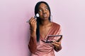 Young african american woman holding makeup brush and blush palette puffing cheeks with funny face