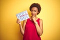 Young african american woman holding menstruation calendar over isolated yellow background serious face thinking about question,