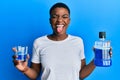 Young african american woman holding mouthwash for fresh breath sticking tongue out happy with funny expression Royalty Free Stock Photo