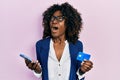 Young african american woman holding smartphone and credit card angry and mad screaming frustrated and furious, shouting with Royalty Free Stock Photo