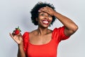 Young african american woman holding strawberry stressed and frustrated with hand on head, surprised and angry face Royalty Free Stock Photo
