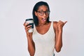 Young african american woman holding take away coffee pointing thumb up to the side smiling happy with open mouth Royalty Free Stock Photo