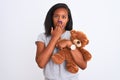 Young african american woman holding teddy bear over isolated background cover mouth with hand shocked with shame for mistake, Royalty Free Stock Photo