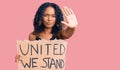 Young african american woman holding united we stand banner with open hand doing stop sign with serious and confident expression, Royalty Free Stock Photo