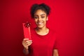 Young african american woman holding valentine gift over isolated red background with a happy face standing and smiling with a Royalty Free Stock Photo