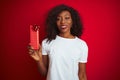 Young african american woman holding valentine gift standing over isolated red background with a happy face standing and smiling Royalty Free Stock Photo