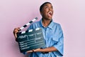 Young african american woman holding video film clapboard angry and mad screaming frustrated and furious, shouting with anger