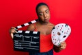 Young african american woman holding video film clapboard and fear mask depressed and worry for distress, crying angry and afraid