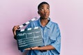 Young african american woman holding video film clapboard making fish face with mouth and squinting eyes, crazy and comical Royalty Free Stock Photo