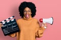 Young african american woman holding video film clapboard and megaphone celebrating crazy and amazed for success with open eyes Royalty Free Stock Photo