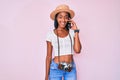 Young african american woman holding vintage camera talking on the smartphone looking positive and happy standing and smiling with Royalty Free Stock Photo