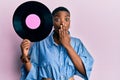 Young african american woman holding vinyl disc covering mouth with hand, shocked and afraid for mistake Royalty Free Stock Photo