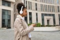 young african american woman hurrying to work listening to music in headphones via mobile phone against the backdrop of Royalty Free Stock Photo