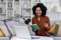 A young African-American woman journalist, blogger conducts a podcast, broadcast remotely from home. Sitting on a sofa Royalty Free Stock Photo