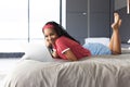 A young African American woman lies on her stomach using a laptop on a bed Royalty Free Stock Photo