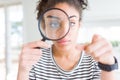 Young african american woman looking through magnifying glass pointing with finger to the camera and to you, hand sign, positive Royalty Free Stock Photo