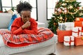 Young african american woman lying on the sofa by christmas tree feeling unwell and coughing as symptom for cold or bronchitis Royalty Free Stock Photo