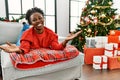 Young african american woman lying on the sofa by christmas tree looking at the camera smiling with open arms for hug Royalty Free Stock Photo