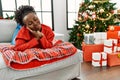 Young african american woman lying on the sofa by christmas tree sleeping tired dreaming and posing with hands together while