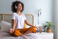 Young woman meditating at home sitting on bed following online meditation, listening with headphones, using phone app. Royalty Free Stock Photo