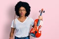 Young african american woman playing violin making fish face with mouth and squinting eyes, crazy and comical