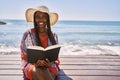 Young african american woman reading book sitting on the bench at the beach Royalty Free Stock Photo