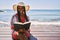 Young african american woman reading book sitting on the bench at the beach Royalty Free Stock Photo