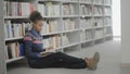 Young african american woman is reading book sitting on floor in university library. Royalty Free Stock Photo