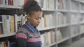 Young african american woman is reading book sitting on floor in university library. Royalty Free Stock Photo