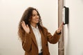 Young African-American woman ringing intercom while waving to camera in entryway