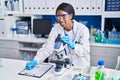 Young african american woman scientist using microscope write on document at laboratory Royalty Free Stock Photo