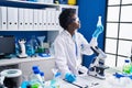 Young african american woman scientist writing on document measuring liquid at laboratory Royalty Free Stock Photo