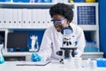 Young african american woman scientist writing on document using microscope at laboratory Royalty Free Stock Photo