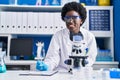 Young african american woman scientist writing on document using microscope at laboratory Royalty Free Stock Photo