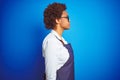 Young african american woman shop owner wearing business apron over blue background looking to side, relax profile pose with Royalty Free Stock Photo