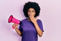 Young african american woman shouting through megaphone covering mouth with hand, shocked and afraid for mistake Royalty Free Stock Photo