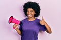 Young african american woman shouting through megaphone smiling happy and positive, thumb up doing excellent and approval sign Royalty Free Stock Photo