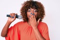 Young african american woman singing song using microphone covering mouth with hand, shocked and afraid for mistake Royalty Free Stock Photo