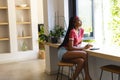 Young African American woman sits at a modern kitchen counter, gazing outside, with copy space Royalty Free Stock Photo