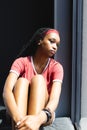 A young African American woman sits by a window, sunlight highlighting her thoughtful expression Royalty Free Stock Photo